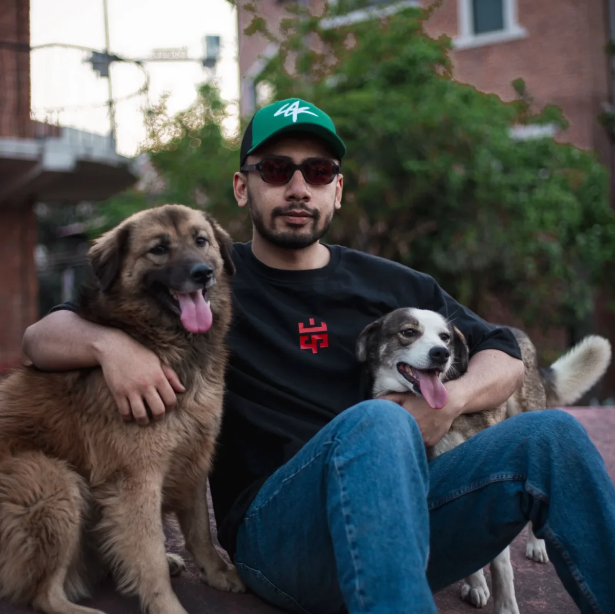Eskecy brand lifestyle photo – model wearing black Eskecy logo tee, sitting outdoors with two dogs